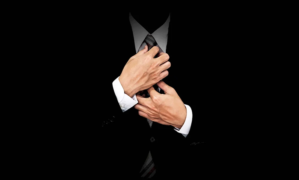 Бизнесмен поправляет галстук на черном фоне